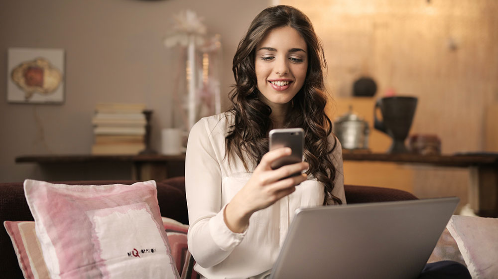 Woman on her couch mobile banking on her cell phone.