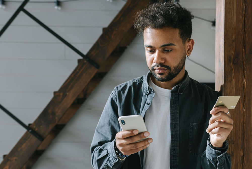 man holding debit card and downloading an app on his phone