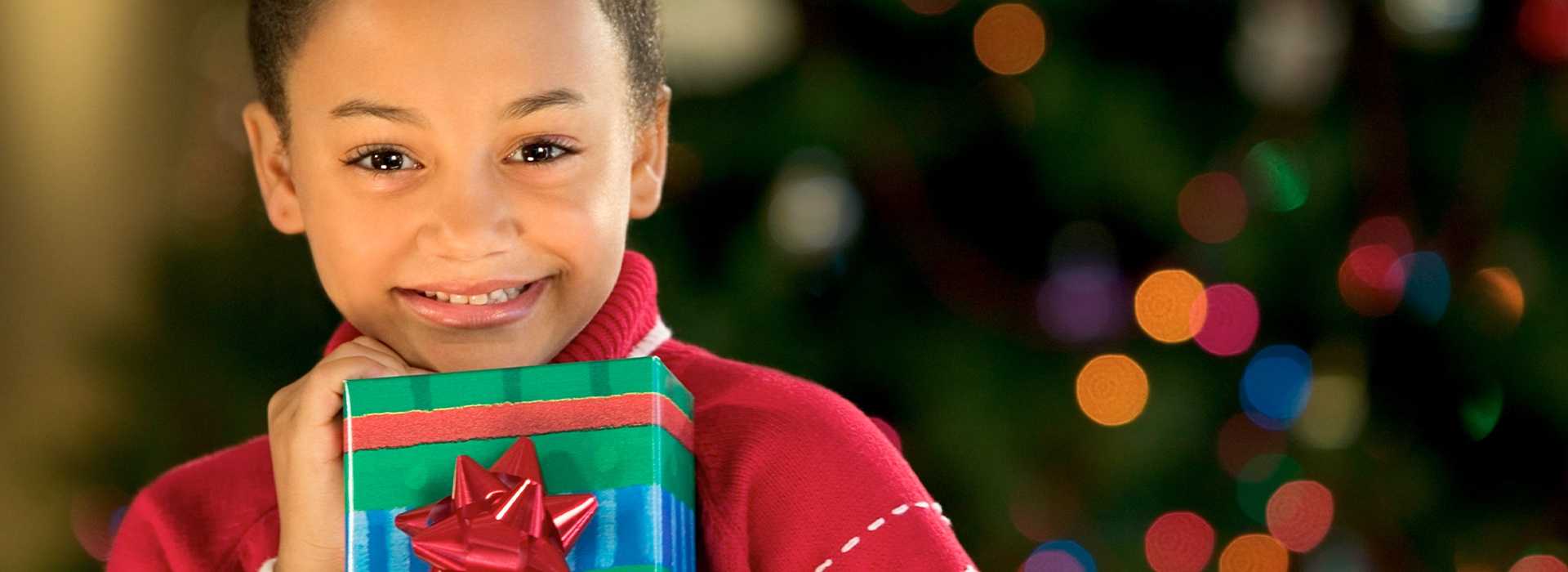 Young girl holding a present in front of a Christmas tree
