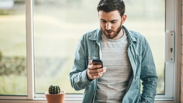 Man leaning against window looking down at his cell phone.